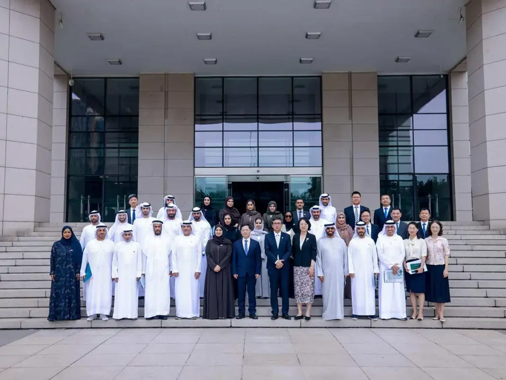 Group photo of the UAE delegation and Chinese officials outside a building during a high-level visit to China, featuring individuals in traditional attire and business suits.