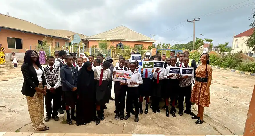 Group of students and teachers in a courtyard, holding signs related to sustainability and the UN's Sustainable Development Goals, with two adults standing next to them.
