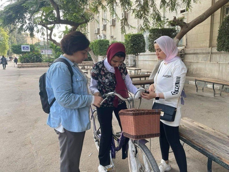 Three women discussing near a bicycle in a public space, highlighting women's empowerment in Cairo.