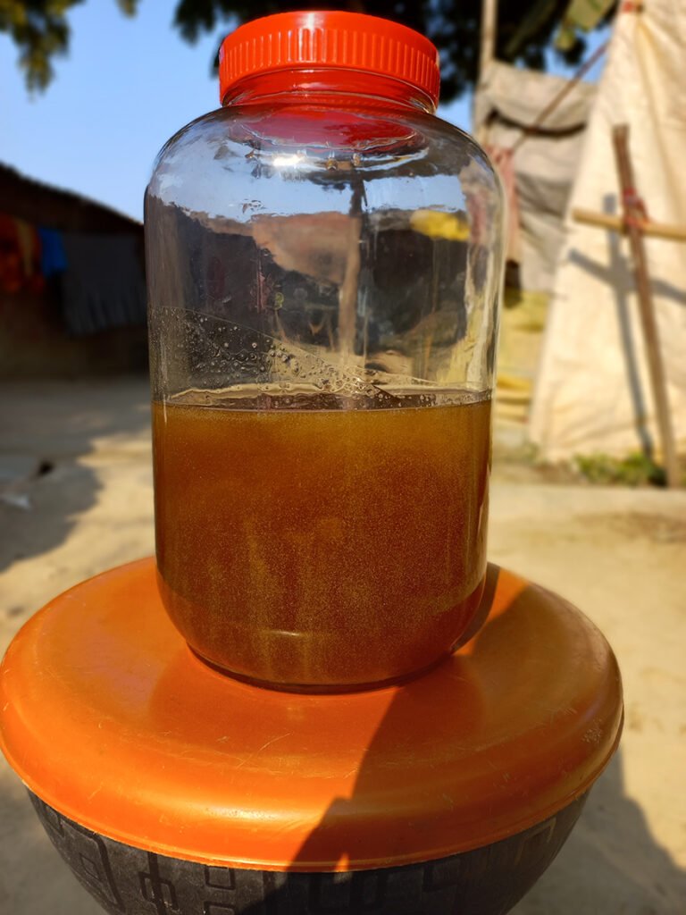 A jar of raw honey with a red cap, placed on a circular orange surface against a blurred outdoor background.