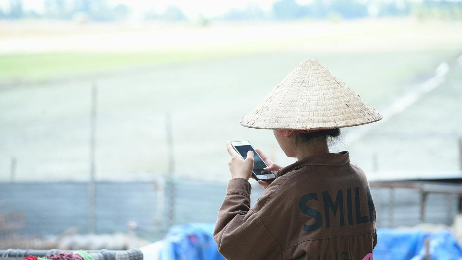 back view of woman holding smartphone in jacket and conical hat