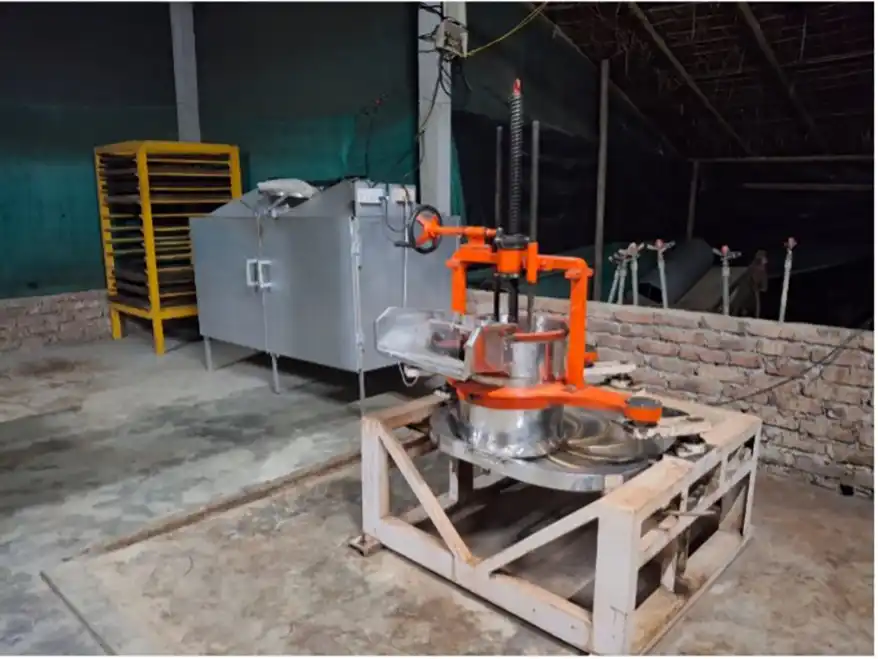 A tea processing machine in an organic tea factory, featuring a silver and orange design, positioned on a wooden platform with a brick wall in the background in Barekuri