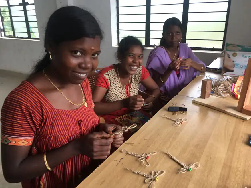 Three women from indigenous communities in Kerala engaged in crafting traditional products at a workshop, showcasing their skills and collaboration.