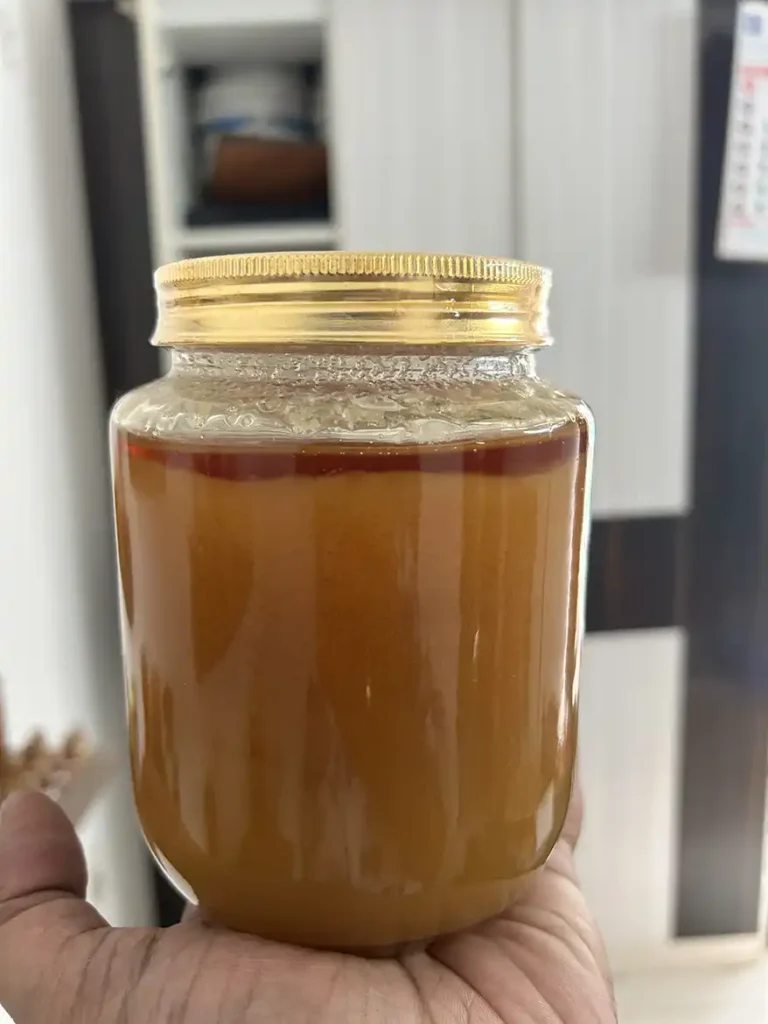 A close-up image of a jar of crystallized honey held in a hand, showcasing its golden-brown color and thick texture.