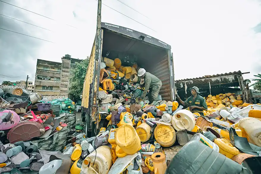 Workers sorting and unloading plastic waste from a truck at a recycling facility.