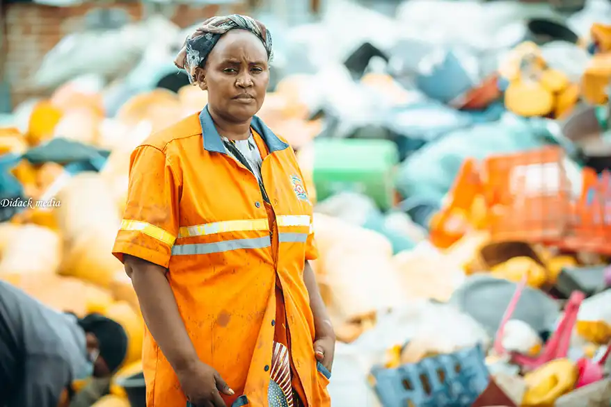 Anita James stands in front of a backdrop of colorful plastic waste, showcasing her role in the recycling process in Mombasa.