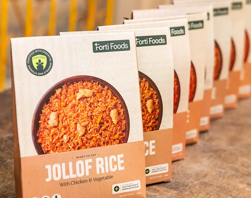 A close-up image of packaged Forti Foods Jollof Rice with Chicken and Vegetable, showcasing the ready-to-eat meal in a bowl on the front of the box, lined up on a surface.