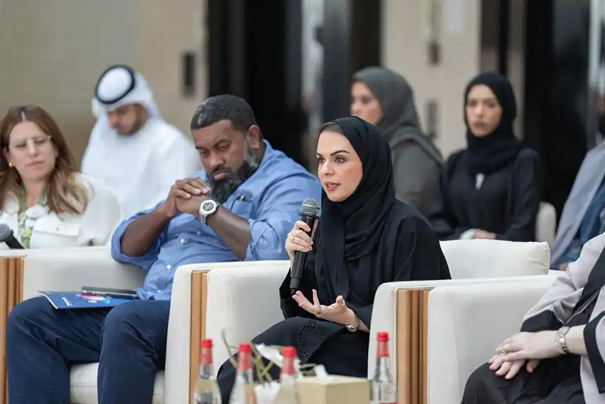 A speaker actively engaging in discussion at the Nature Guardians Majlis, surrounded by audience members in a formal setting.