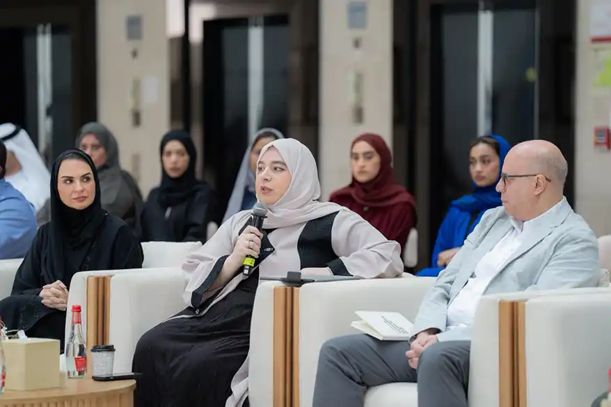 A diverse group of participants engaged in discussion at the Nature Guardians Majlis, with a woman speaking into a microphone and seated individuals in traditional attire listening attentively.