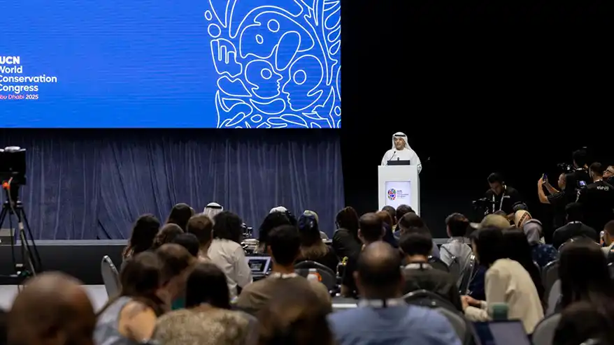 A speaker addresses an audience at the IUCN World Conservation Congress in Abu Dhabi, UAE, with a large screen displaying event branding in the background.