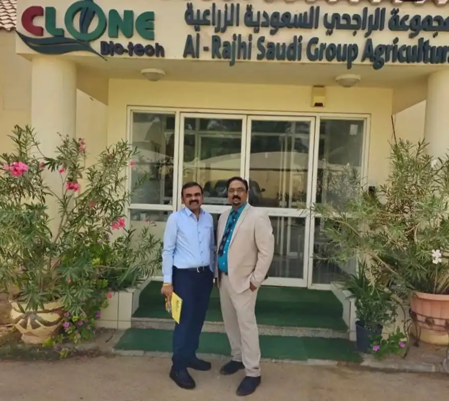 Two men standing in front of the Clone Bio-Tech office, with a plant and flowers in the foreground.