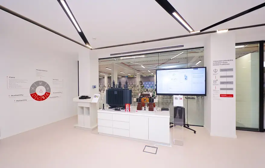 Interior view of the ABB Customer Experience Center showcasing digital energy management tools, a workshop area with models, and a large screen displaying monitoring data.