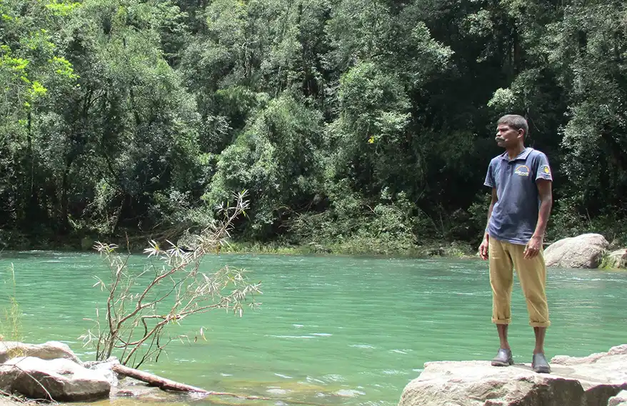 Maari, a Muduga tribesman stands on a rock by the Kunthipuzha River in Kerala's Silent Valley, surrounded by lush green forest.