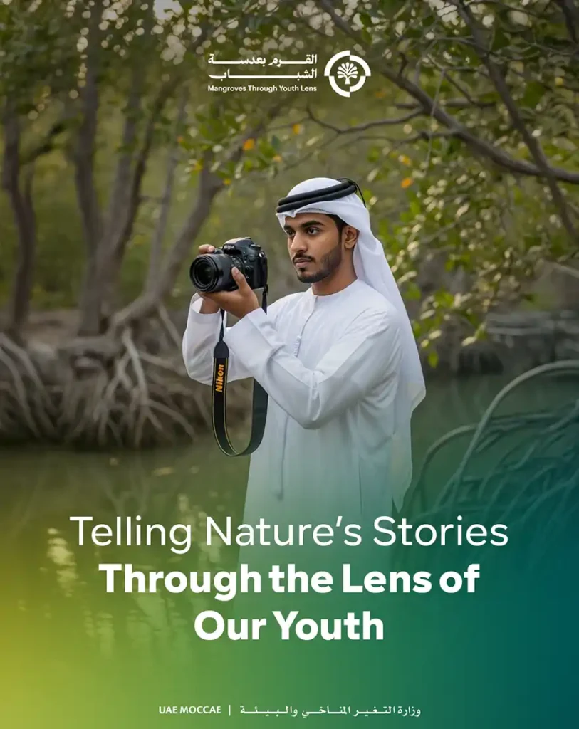A young man dressed in traditional Emirati attire holding a Nikon camera, standing in a mangrove forest, with the text 'Telling Nature's Stories Through the Lens of Our Youth' overlaying the image.