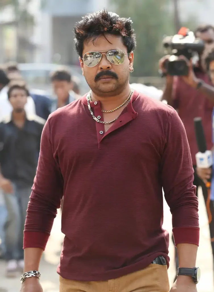 A man walking confidently in a maroon long-sleeve shirt and sunglasses, with a mustache and accessories, surrounded by a crowd.