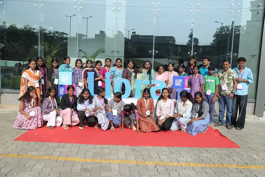 Group photo of participants posing in front of a large colorful sign that says 'Libra', on a red carpet near a glass building.