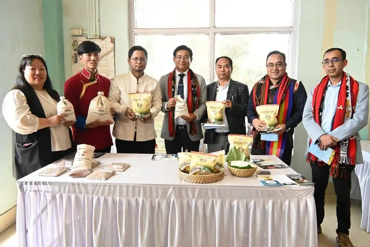 Group of individuals holding various packaged food products, standing behind a table with more items displayed, in a bright room with large windows.