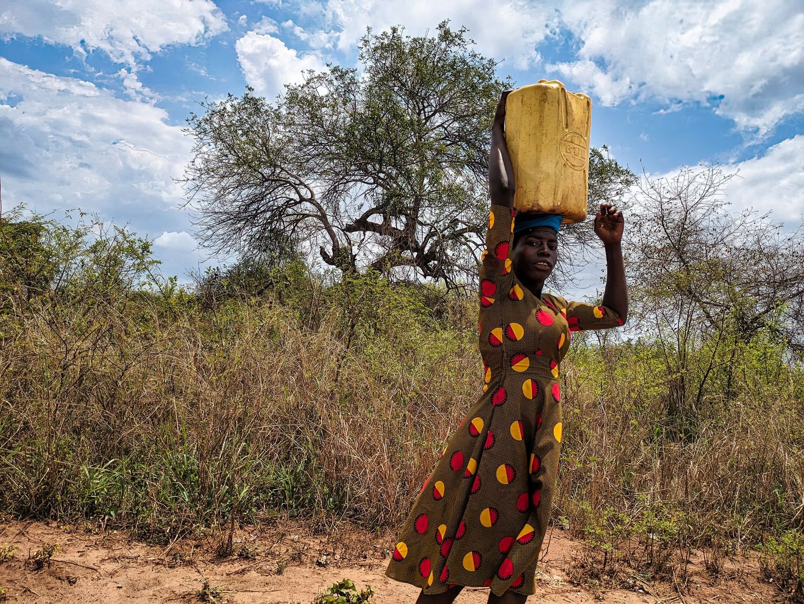 woman in patterned dress carrying container on head