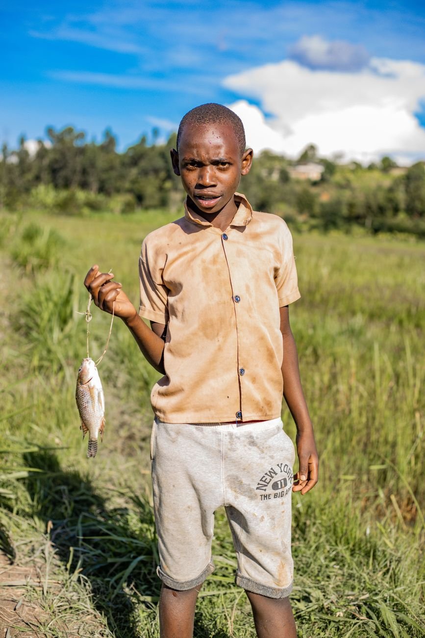 boy holding fish in a rural grassland setting