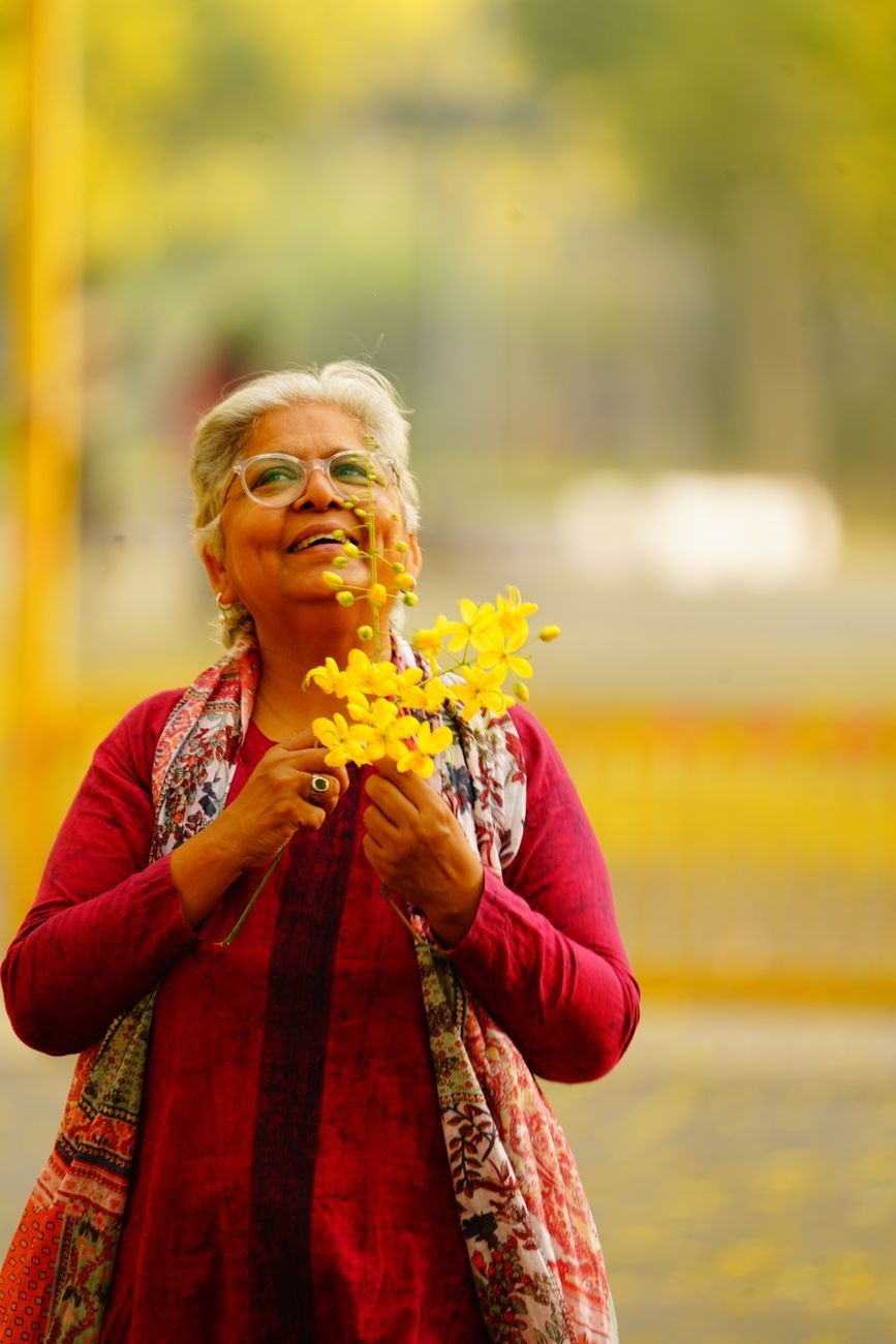 elderly woman joyfully holding yellow flowers outdoors