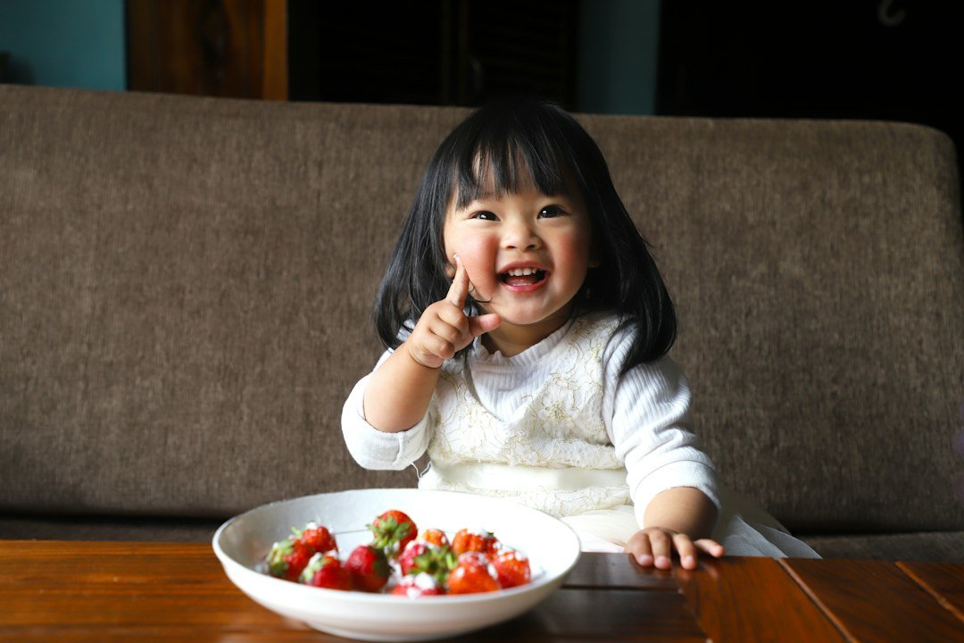 A young child sits with a bowl of fresh fruit