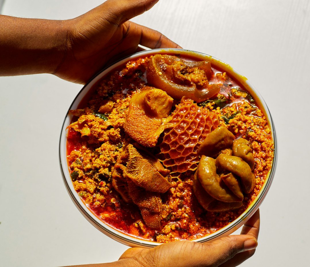 Hands holding a bowl of egusi soup with assorted meats