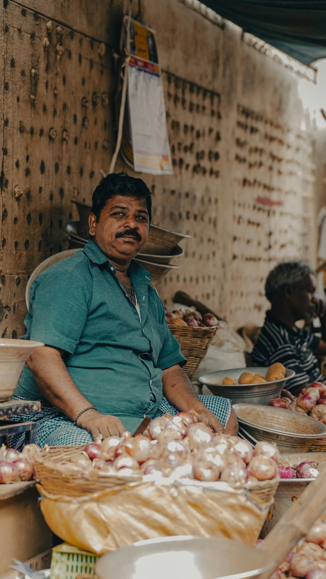 Market vendor sitting with baskets of fresh onions