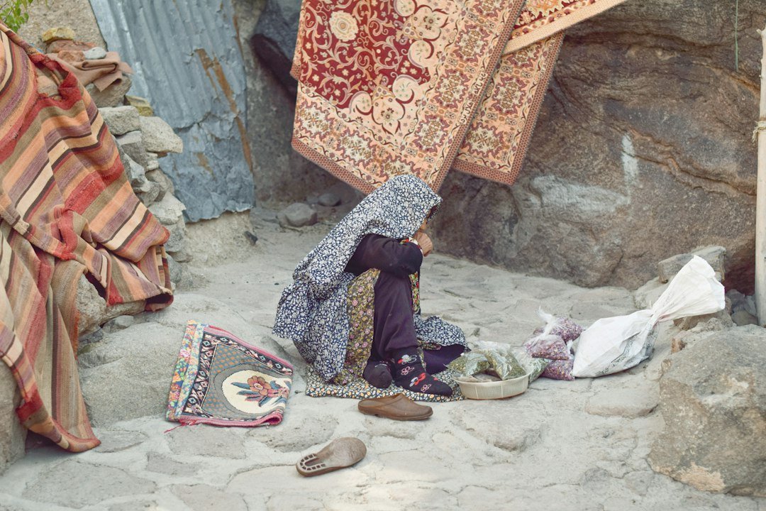 A woman sits on the ground with rugs and goods for sale
